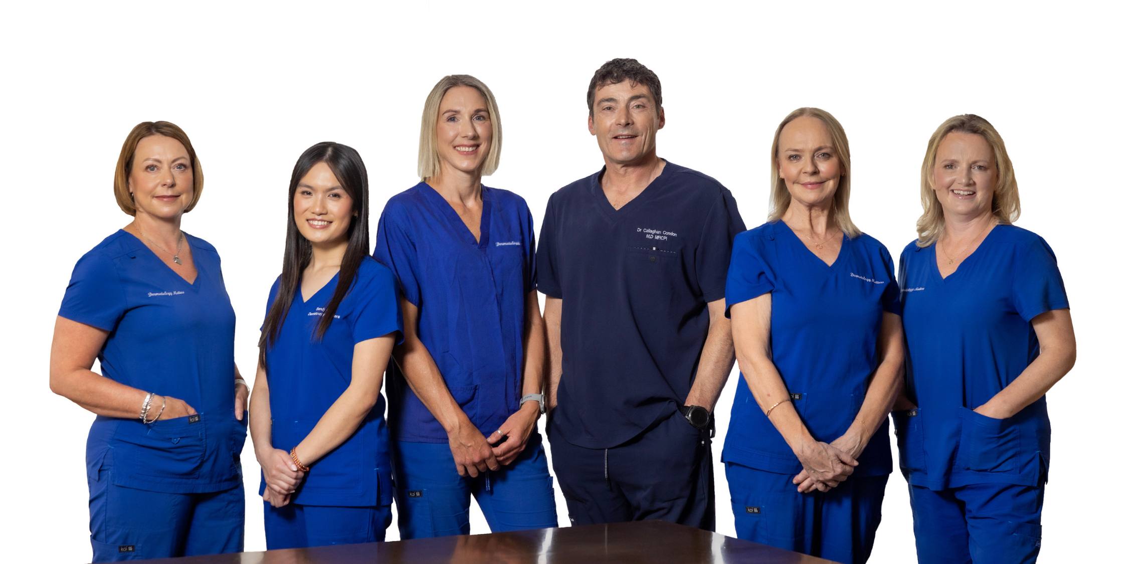Group of six people in blue scrubs posing together on a white background